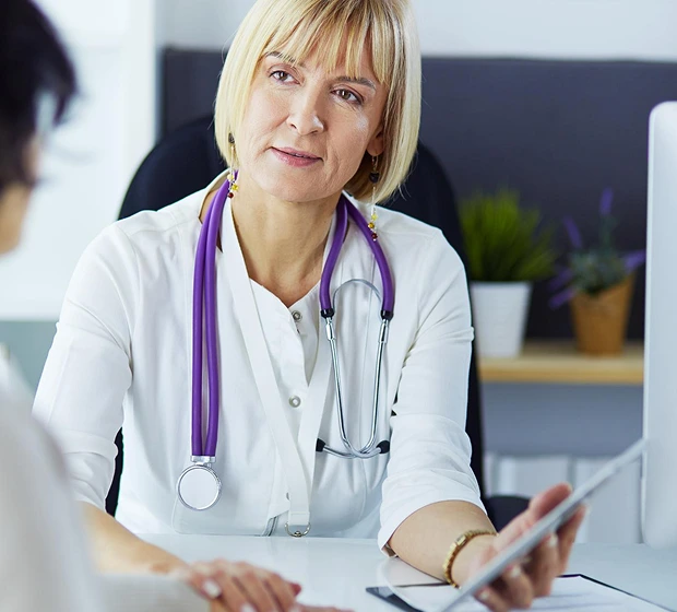 A female doctor with a purple stethoscope listens attentively to a patient, creating a reassuring and professional atmosphere in a medical office.